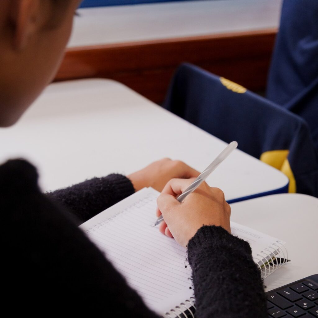 :Aluna uniformizada fazendo anotações em caderno durante aula em unidade de franquia educacional 