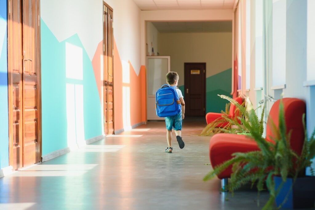 Aluno com mochila azul correndo em corredor colorido de escola, ilustrando artigo sobre franquia de escola particular com ambiente acolhedor para crianças