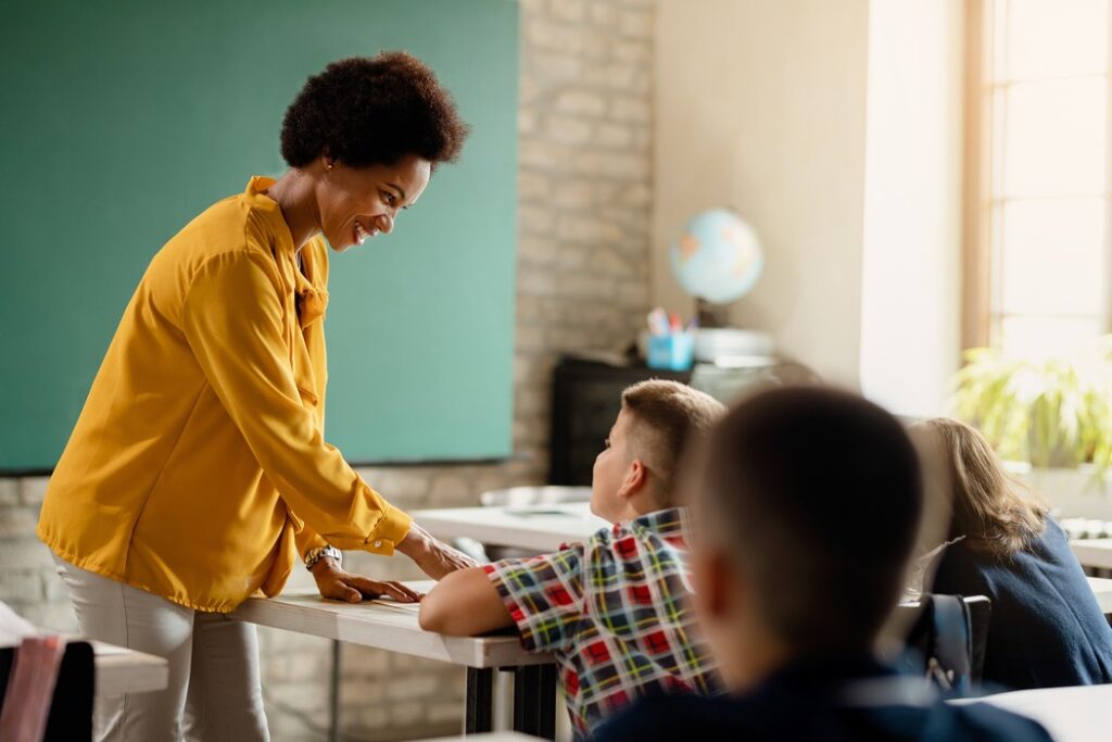 Professora interagindo com aluno em sala de aula, representando a qualidade de ensino oferecida por franquias de educação.